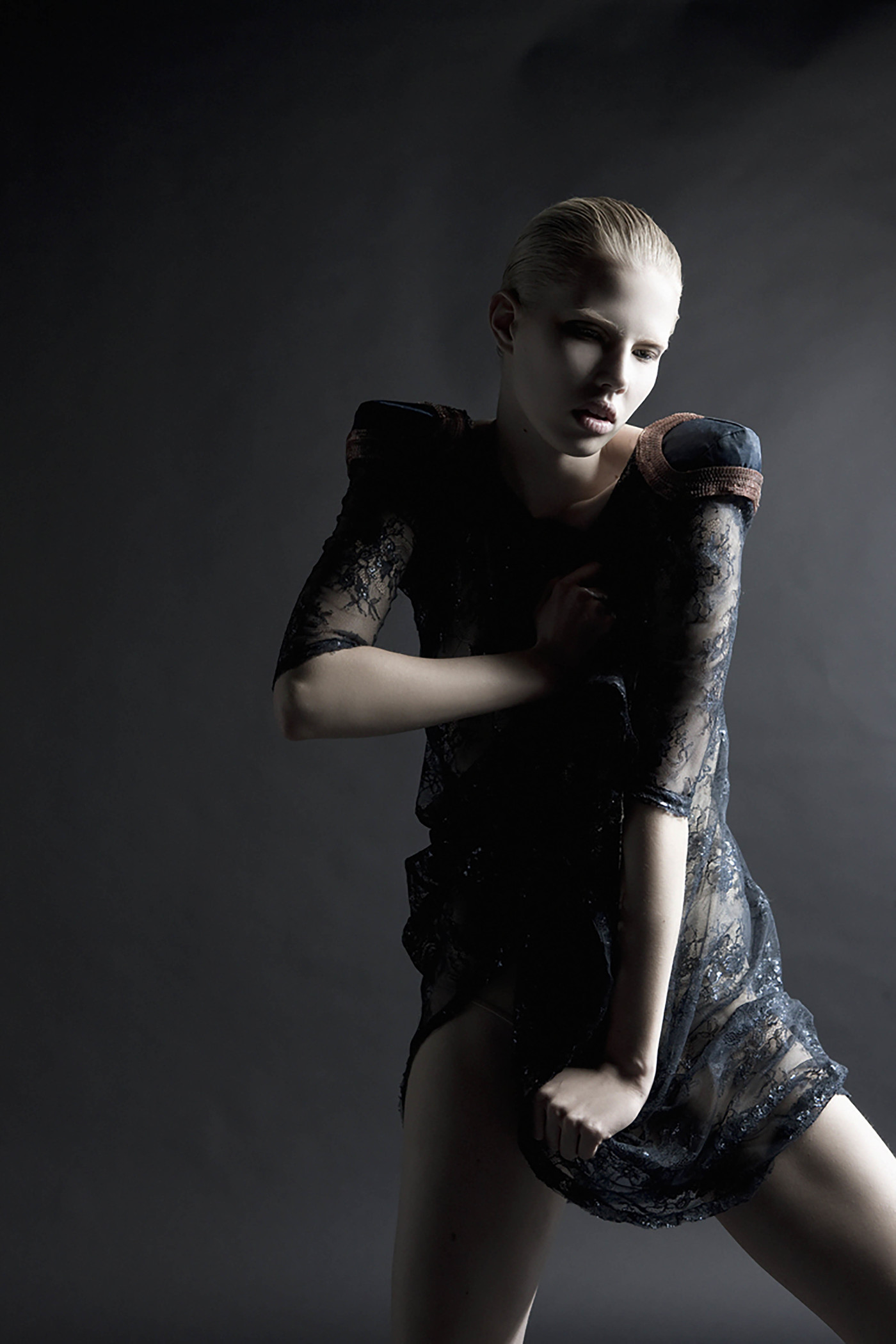 Studio shot of woman in a black lace dress with wet hair, posing against a dark grey background with dramatic lighting and cool color palette.