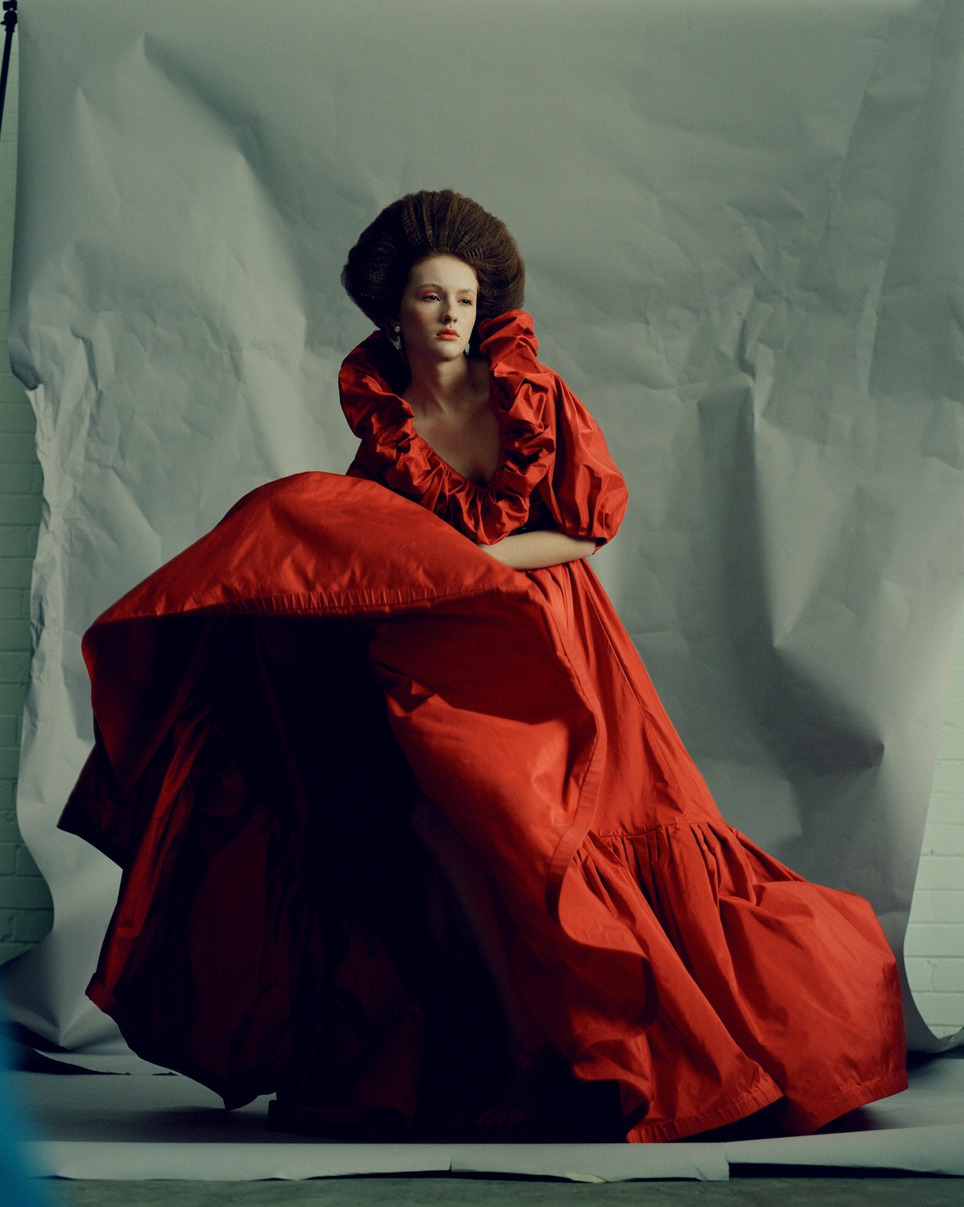 Adult woman in a theatrical pose wearing a voluminous, ruffled red gown with a large afro-style hairstyle in a studio setting.