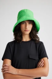 A woman wearing a vibrant green bucket hat and a black t-shirt with crossed arms against a plain white background.