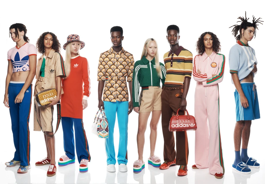 A diverse group of models pose in an indoor studio setting, showcasing a collaborative fashion line featuring apparel and accessories with bold color blocks and retro styles.