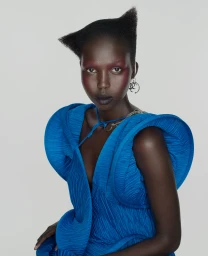 Model with sculptural haircut wearing a vibrant blue dress against a plain white background