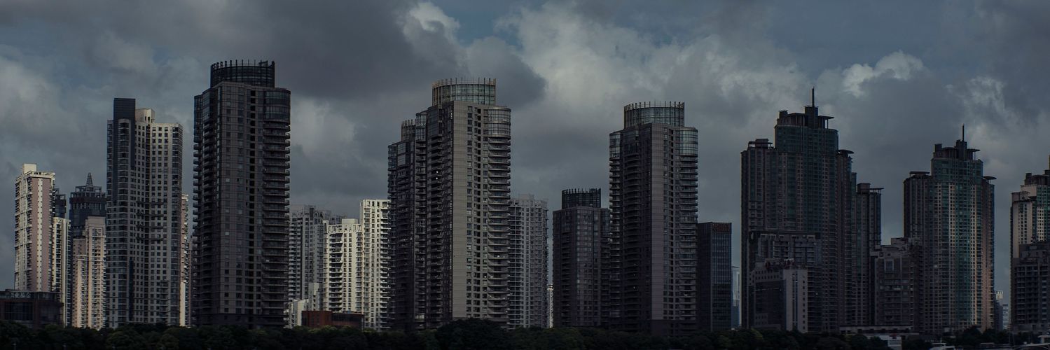 Panoramic view of a city skyline featuring several high-rise buildings under a cloudy, overcast sky, creating a dramatic urban landscape.