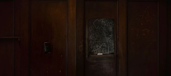 Dark wood paneled wall featuring a small inset chalkboard with children's chalk drawings.