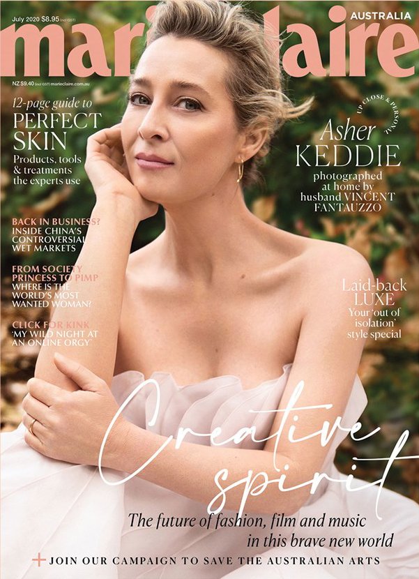 Asher Keddie graces the cover of Marie Claire Australia, July 2020 issue. She wears a white dress and poses against a leafy background.