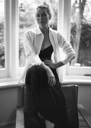 Monochrome portrait of a woman in a white button-down shirt and dark skirt seated by a window styled by Tessa Law.