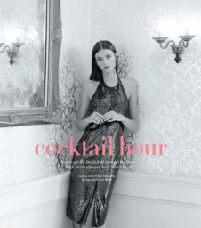 Model leaning against patterned wall wearing a dark halter dress, with ornate wall sconces and a large framed mirror.