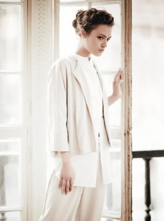 Woman in cream jacket and white shirt posing near a large window, with makeup by Lei Tai in Sydney.
