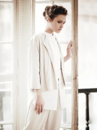 Woman in cream jacket and white shirt posing near a large window, with makeup by Lei Tai in Sydney.