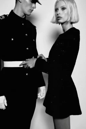 Fashion shot in black and white of male in military dress uniform placing hand on shoulder of woman in sparkly black dress.