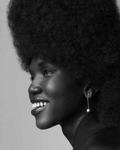 Black and white portrait of a smiling African woman with an afro hairstyle, wearing a black top and a silver earring.