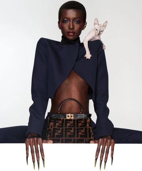 Elegant portrait of a Black woman in blue suit with cat on her shoulder, holding a Fendi purse, against a clean white backdrop.