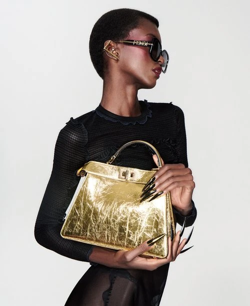 Fashionable Black model presents golden Fendi handbag with black manicure in studio shot with Fendi sunglasses and black long-sleeve dress.