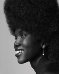 Black and white profile portrait of a smiling Black woman with a large afro hairstyle and dangling drop earrings by Pete Lennon.