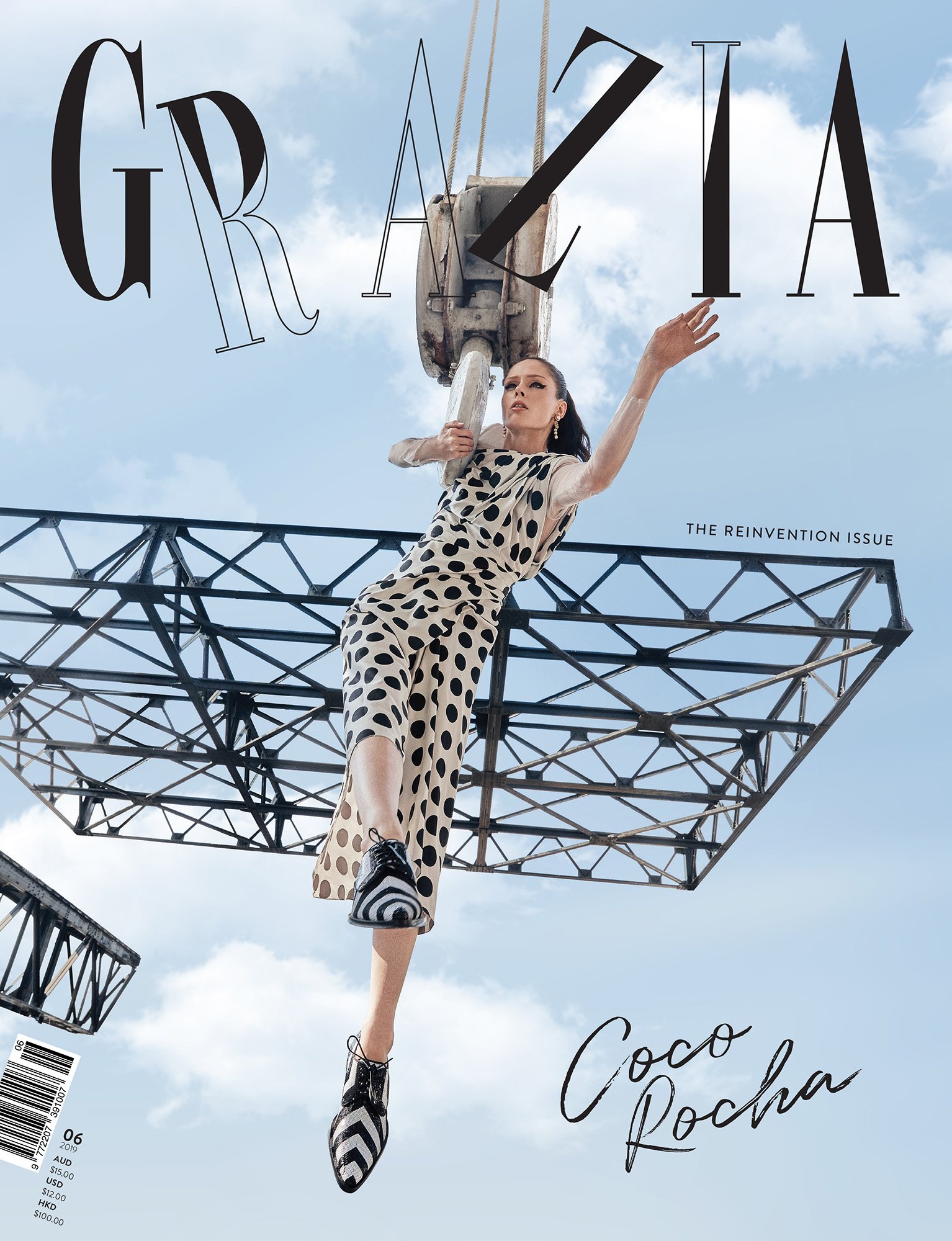 Fashion editorial magazine cover featuring a woman in a polka dot dress hanging from a crane under a blue sky with the magazine's title.