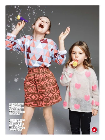 Two young girls play with bubbles in a studio. One girl wears a patterned sweater and skirt; the other wears a heart-themed sweater.