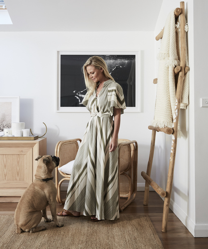 Woman in a striped dress and a brown dog are indoors in a living room with neutral decor, featuring a wooden blanket ladder.