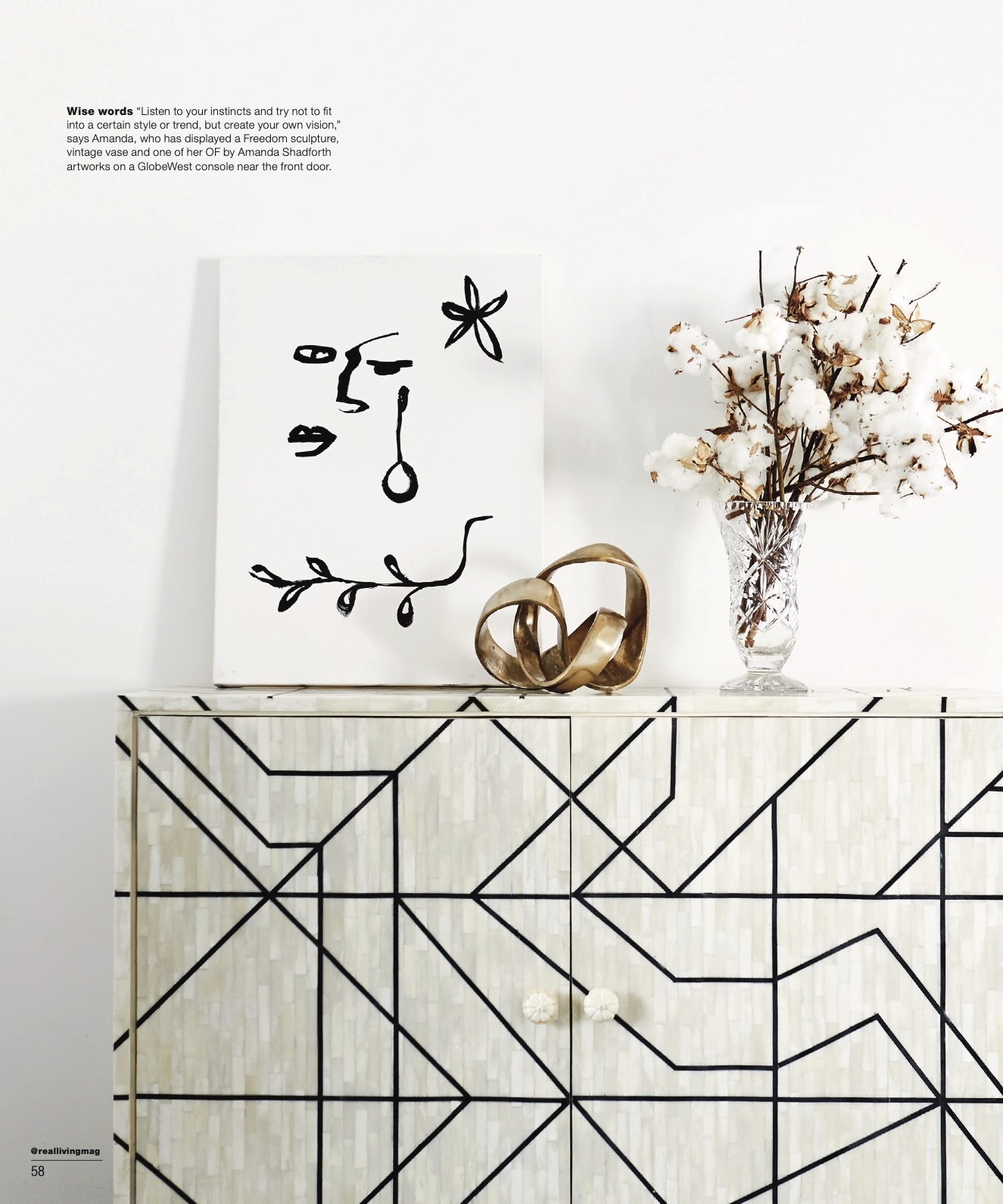 Modern living room interior featuring a geometric cabinet, an abstract painting, and a vase with cotton branches against a white wall.
