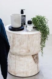 A wooden stump stool topped with a candle, perfume bottle, lotion pump, and trailing string of pearls plant.
