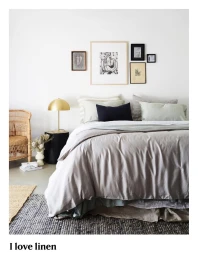 Styled double bed with grey linen duvet and stacked pillows against a white wall with a gallery of framed artwork above