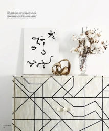 Console table with geometric pattern displaying abstract art, gold sculpture, and cotton stems in vase