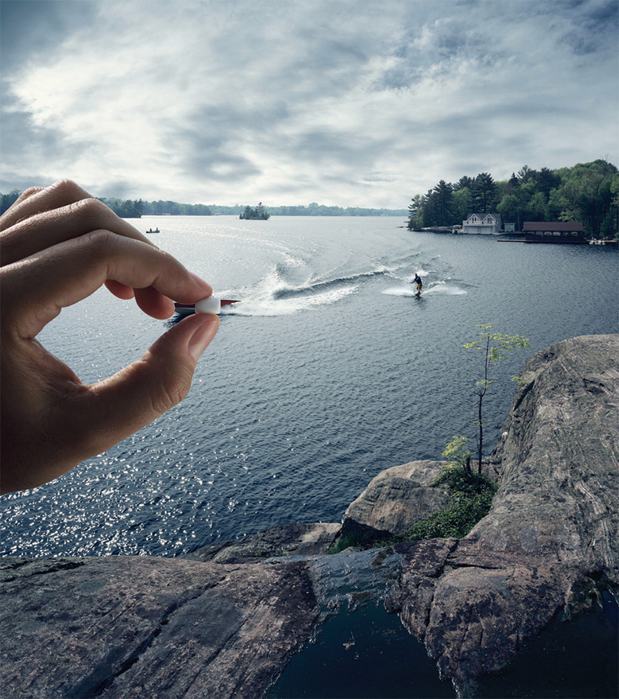 Waterskier glides across a blue lake, captured in a creative composition with a hand holding a miniature representation of the scene.