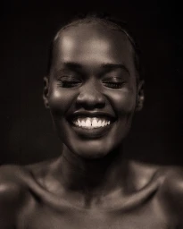 Close-up portrait of a smiling Black woman with closed eyes against a dark background, photographed by Hector Clark.