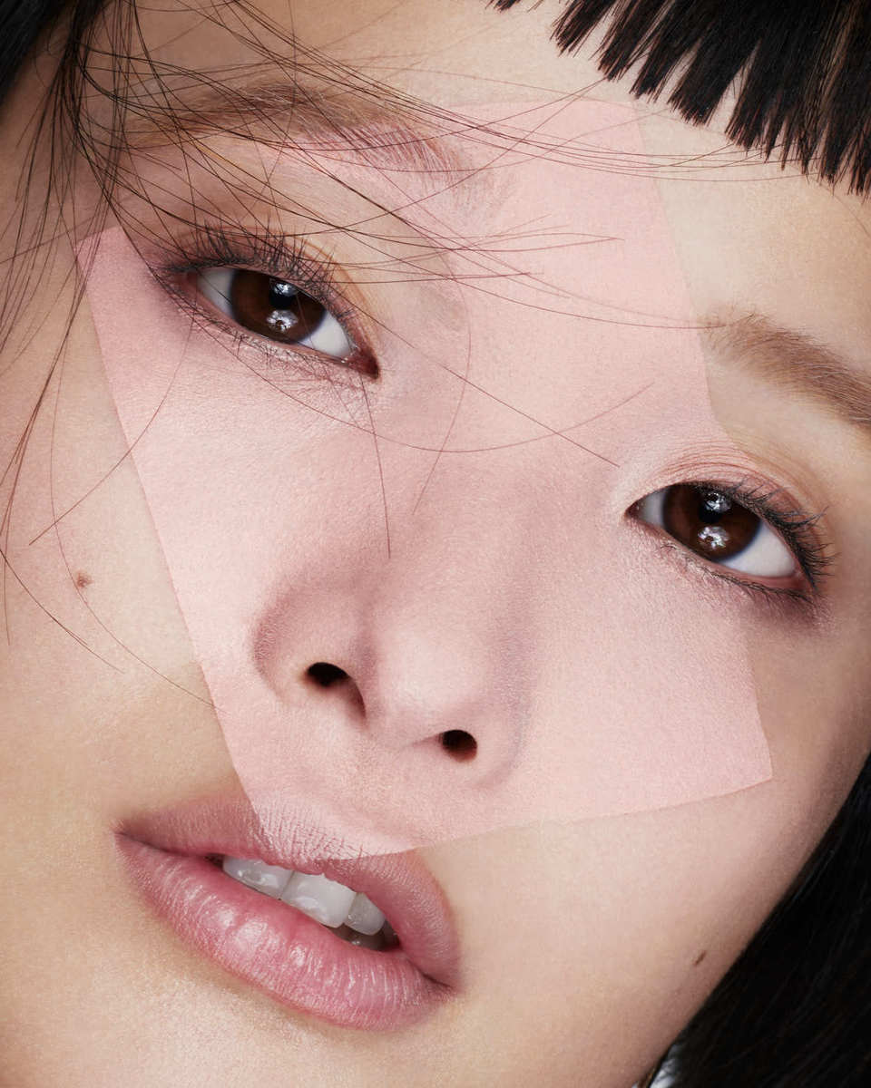 Close-up beauty shot of an Asian woman with dark hair and pink geometric shapes over her face, highlighting makeup and features.