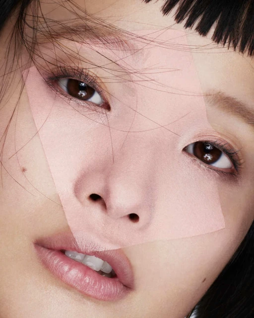Close-up beauty shot of an Asian woman with dark hair and pink geometric shapes over her face, highlighting makeup and features.
