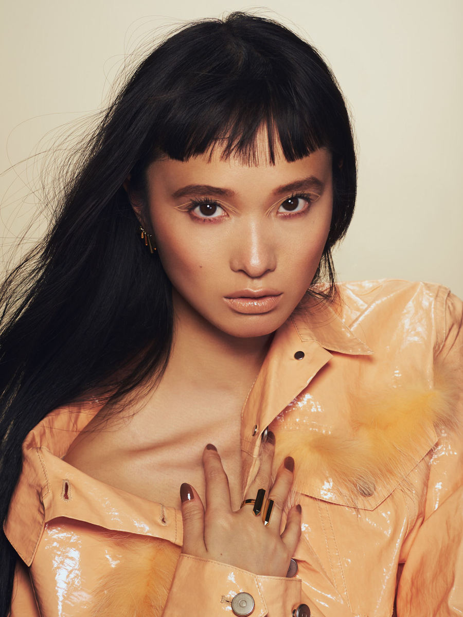 Portrait of an Asian woman with black hair and peach-colored jacket. Close-up shot with neutral background. Fashion or beauty style.