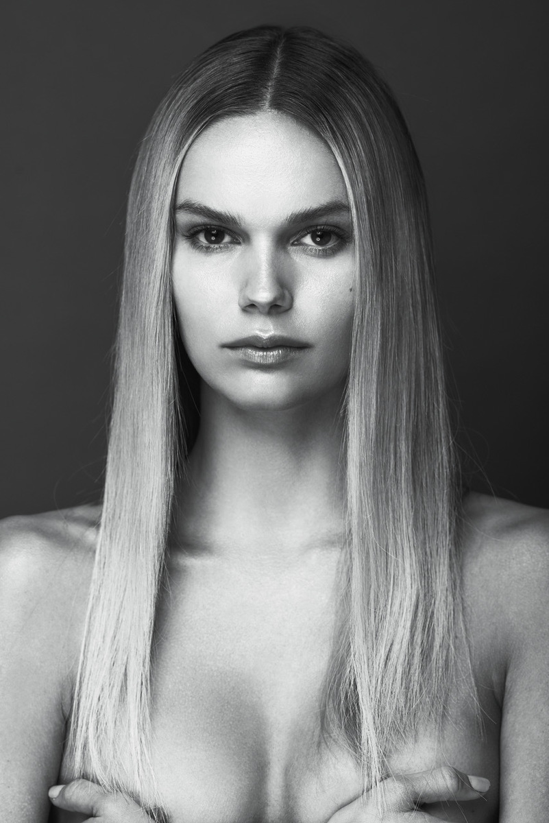 Black and white portrait of a fair-skinned woman with long blonde hair, posing in front of a dark gray background.
