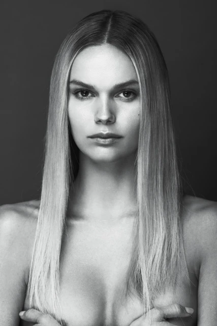Black and white portrait of a fair-skinned woman with long blonde hair, posing in front of a dark gray background.