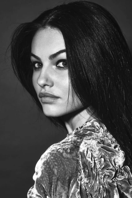 Portrait of a brunette woman with long hair, gazing over her shoulder, wearing a velvet top against a plain background in black and white.