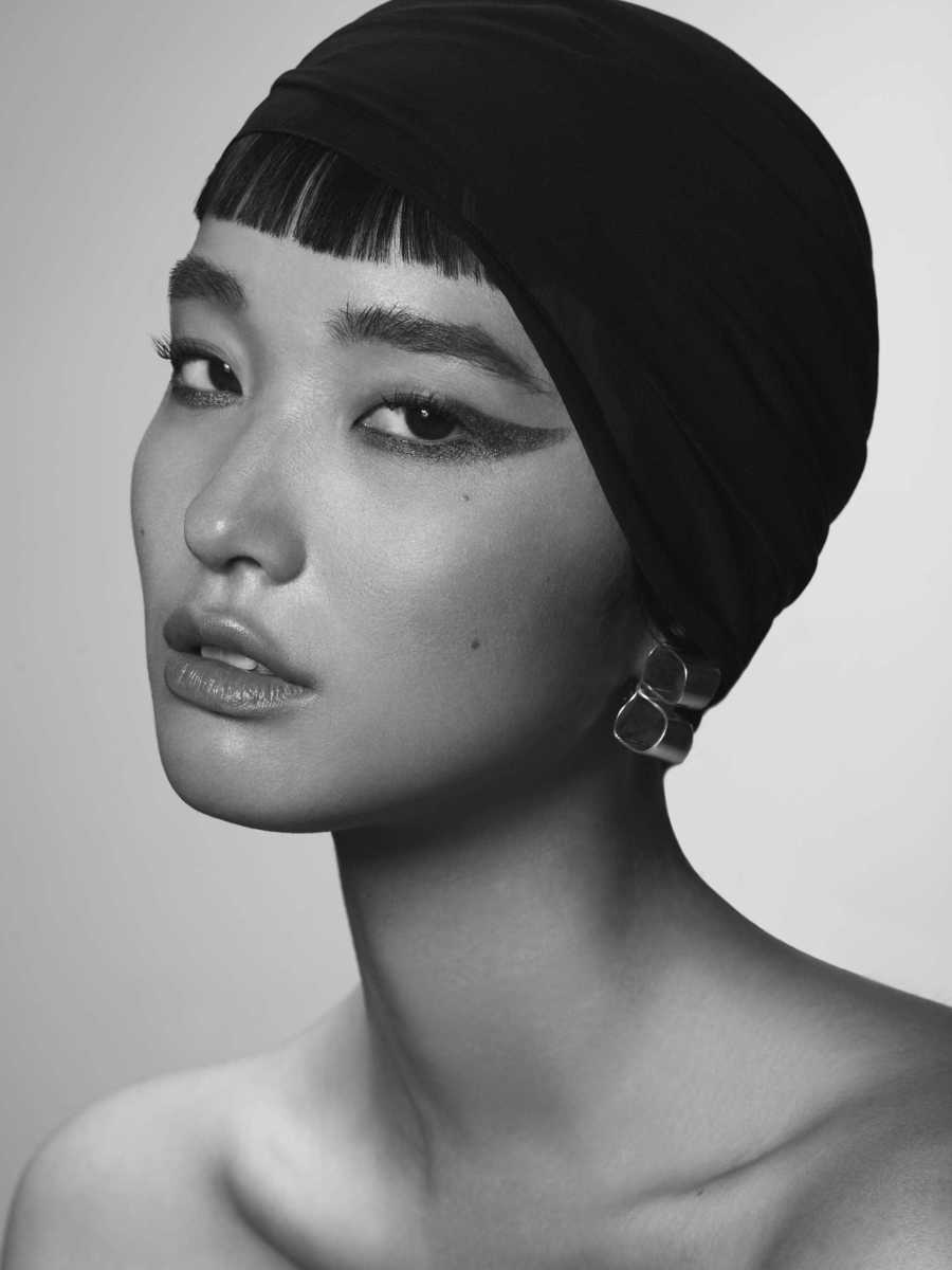 Close-up portrait of a woman wearing a dark fitted headwrap and dramatic winged eyeliner by Rayan Ayash