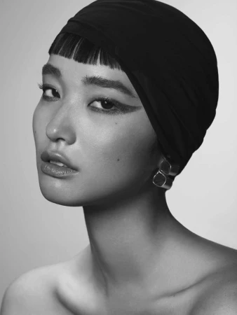 Close-up portrait of a woman wearing a dark fitted headwrap and dramatic winged eyeliner by Rayan Ayash