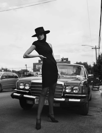 Monochrome fashion editorial featuring a woman in a black hat and dress posing in front of a vintage car