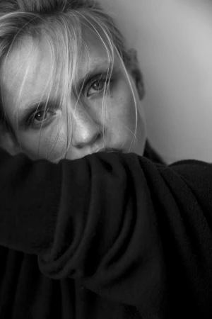 Close-up monochrome portrait of a woman with blonde hair across her face, resting her chin on her arm.