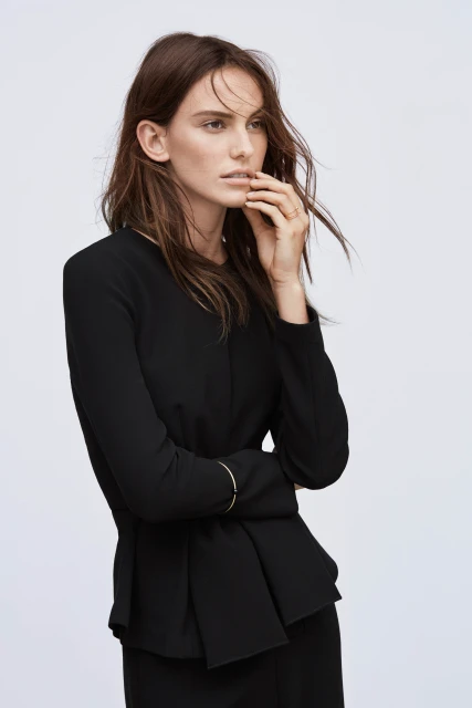 Portrait of an adult woman in a black peplum top and skirt against a white background in a fashion photography setting.