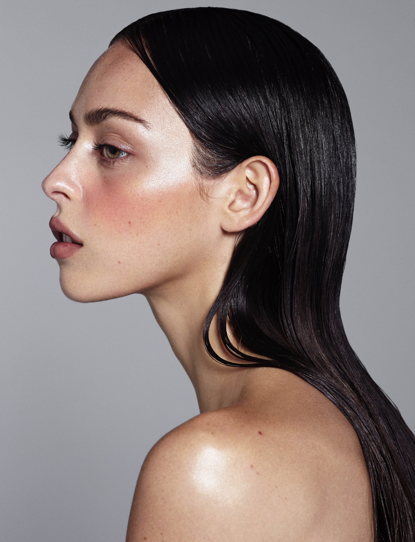 Profile shot of a fair-skinned woman with long, dark, shiny hair against a light gray background, showcasing beauty and fashion elements.
