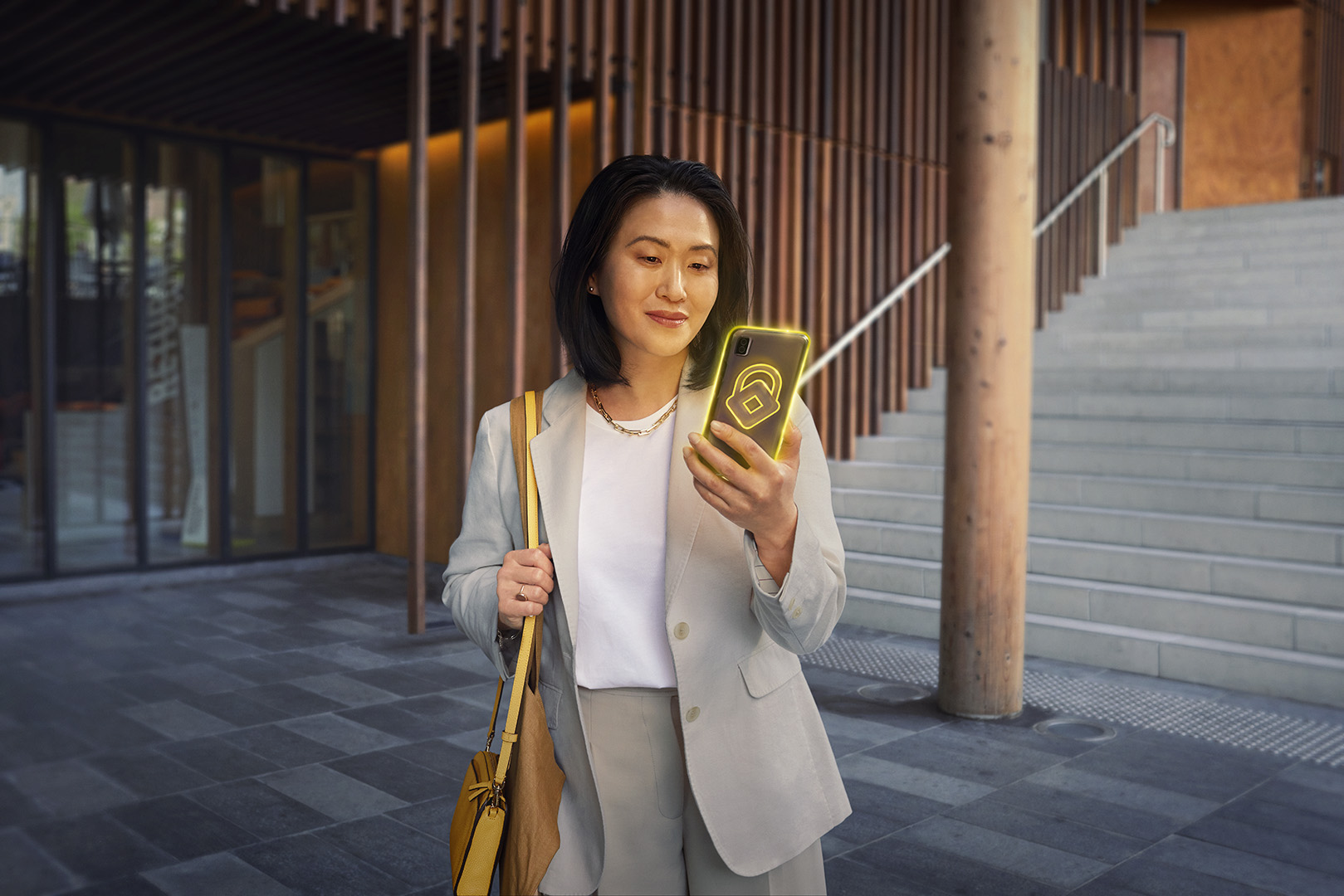 An Asian woman in a blazer is standing outdoors, holding a smartphone with a lock icon. She has a purse over her shoulder.