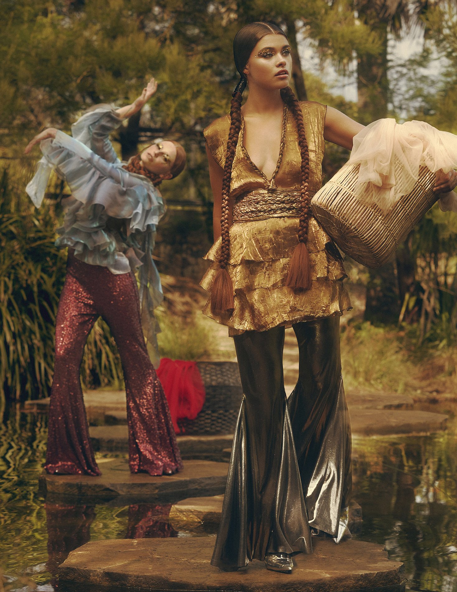 Two women pose outdoors in bohemian-style clothing. One woman wears gold and silver, while the other wears blue and maroon tones.