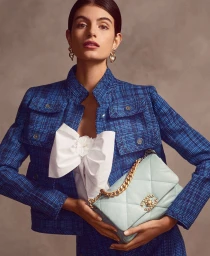 Woman wearing blue tweed jacket holding light blue quilted handbag with gold chain strap in Sydney studio