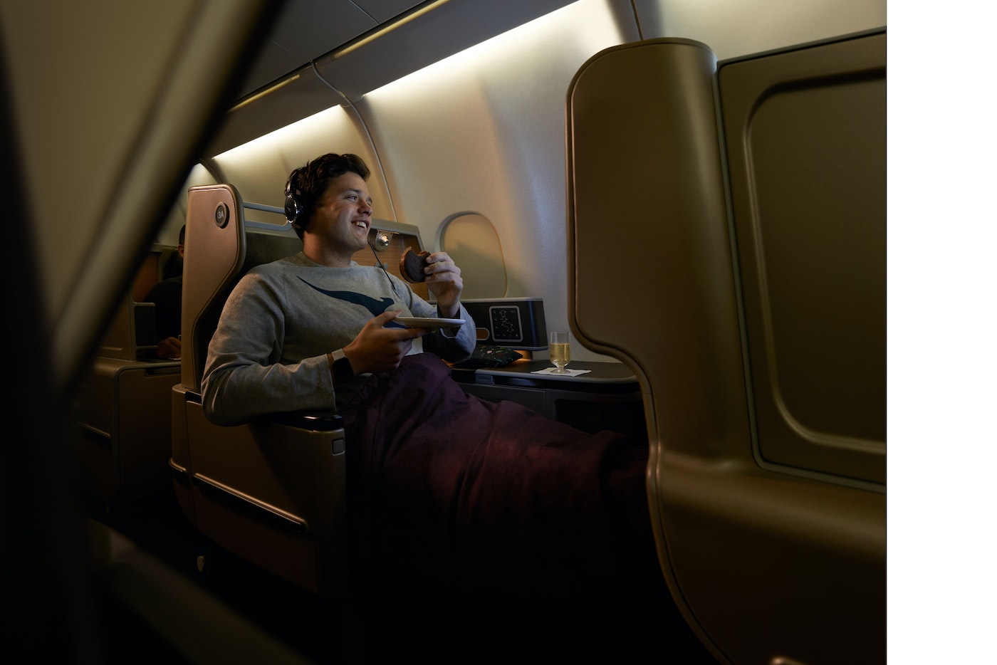 Man enjoys drink on a luxury airplane in business class seating. Overhead lights illuminate the cabin during inflight service.