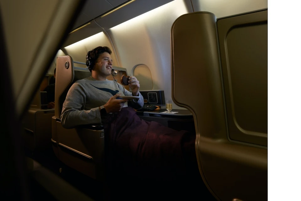 Man enjoys drink on a luxury airplane in business class seating. Overhead lights illuminate the cabin during inflight service.