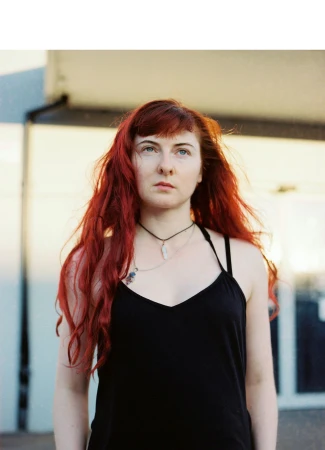 Portrait of a young woman with long red hair wearing a black top and pendant necklaces outdoors