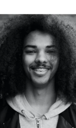 Portrait of smiling young Black man with voluminous afro hair wearing a hooded sweatshirt and dark jacket