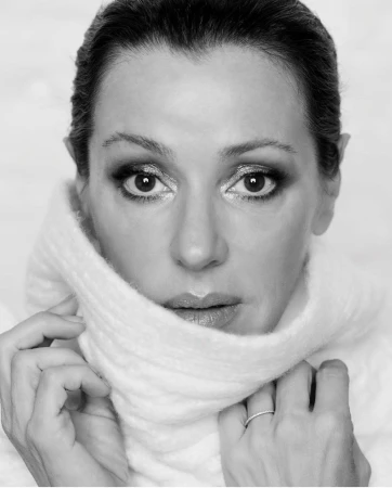Close-up monochrome portrait of a woman pulling up a white high-neck sweater, styled by hair stylist Tanya Guccione
