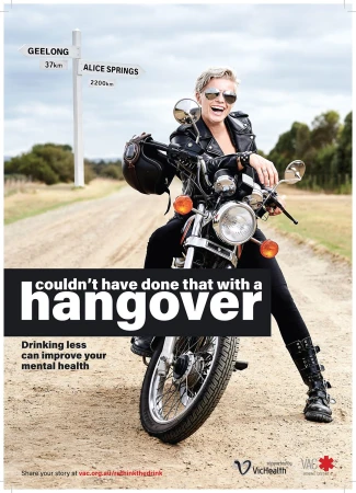 Smiling woman in sunglasses and black leather jacket sitting astride a motorcycle on a dusty road with a directional sign post in the background.