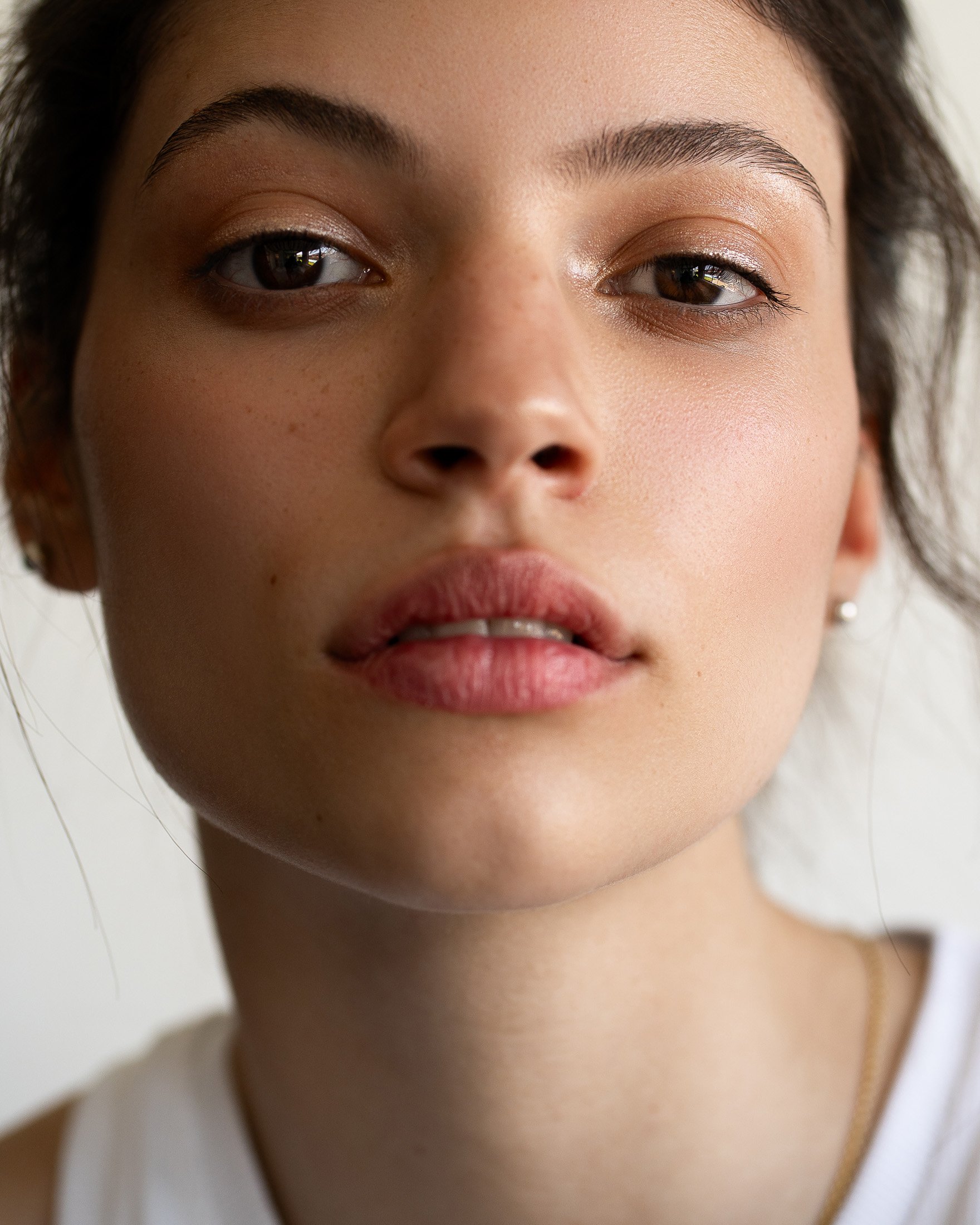 Close-up portrait of a young adult female with neutral expression. The focus is on her face, showcasing natural beauty in soft lighting.