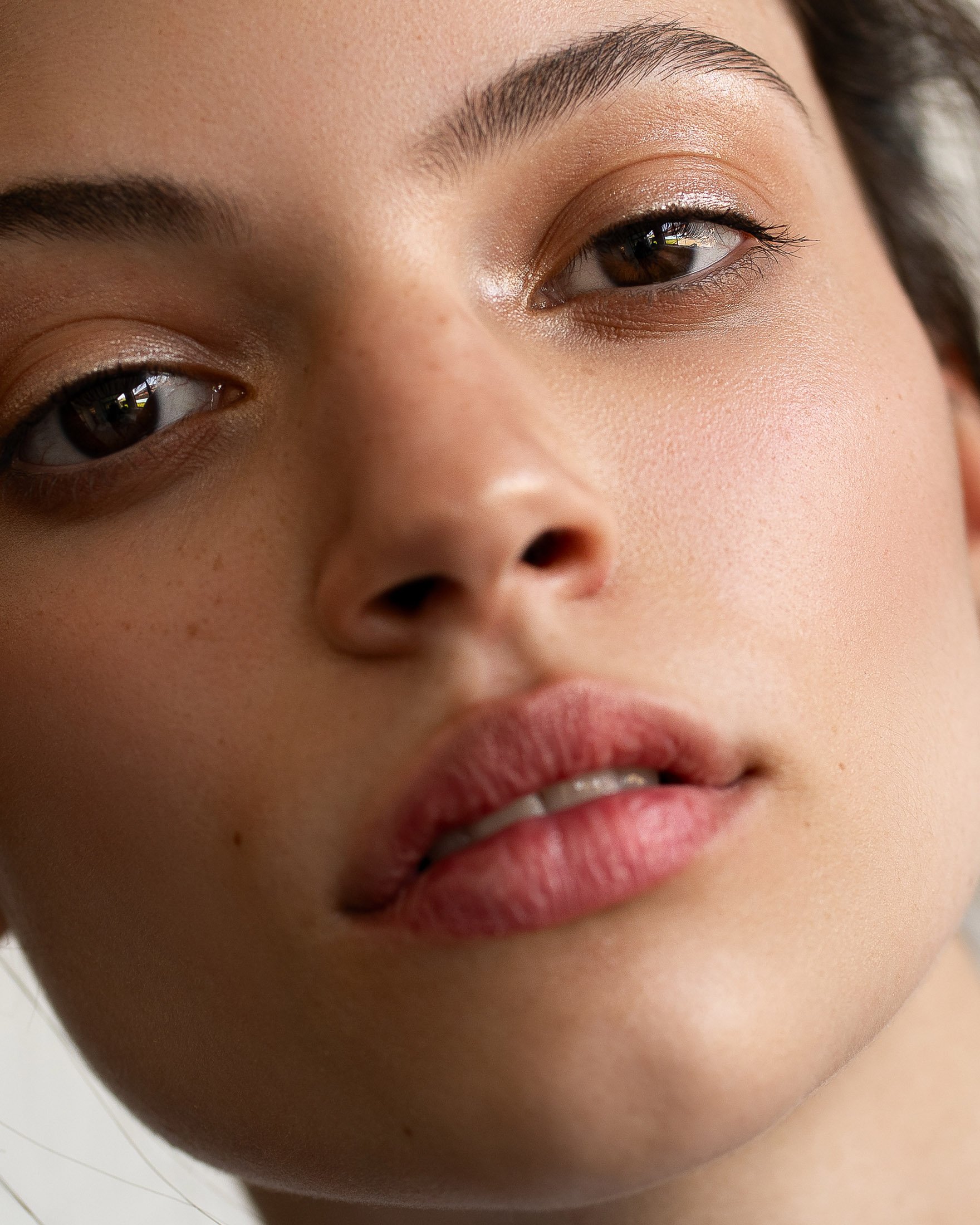 Close-up shot of a young adult woman with light skin, brown eyes, and pink lips. Beauty shot with natural make-up and indoor lighting.