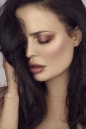 Close-up portrait of a woman with dark wavy hair and muted mauve eyeshadow, styled by Tanya Guccione.